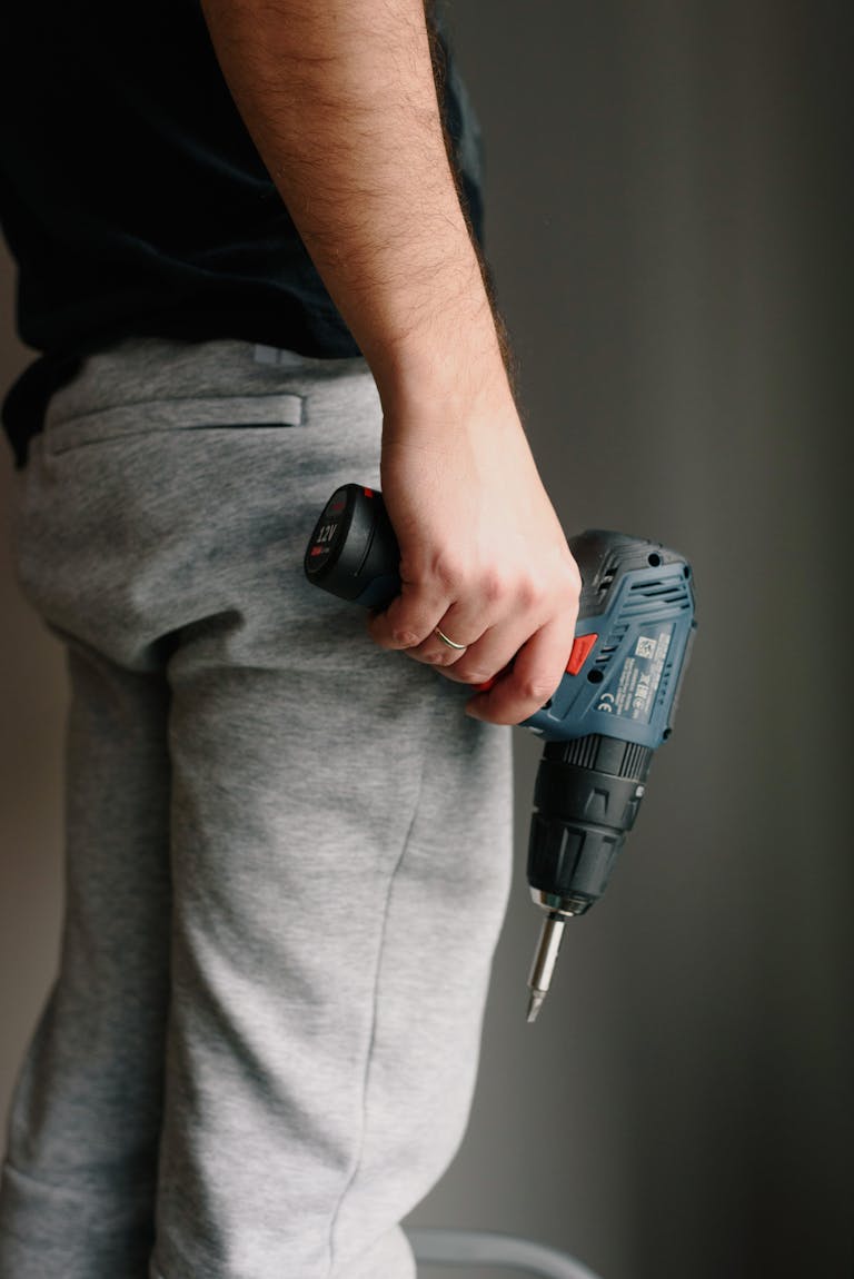 A man holds a cordless drill, ready for installing a ring alarm, against a neutral indoor background.