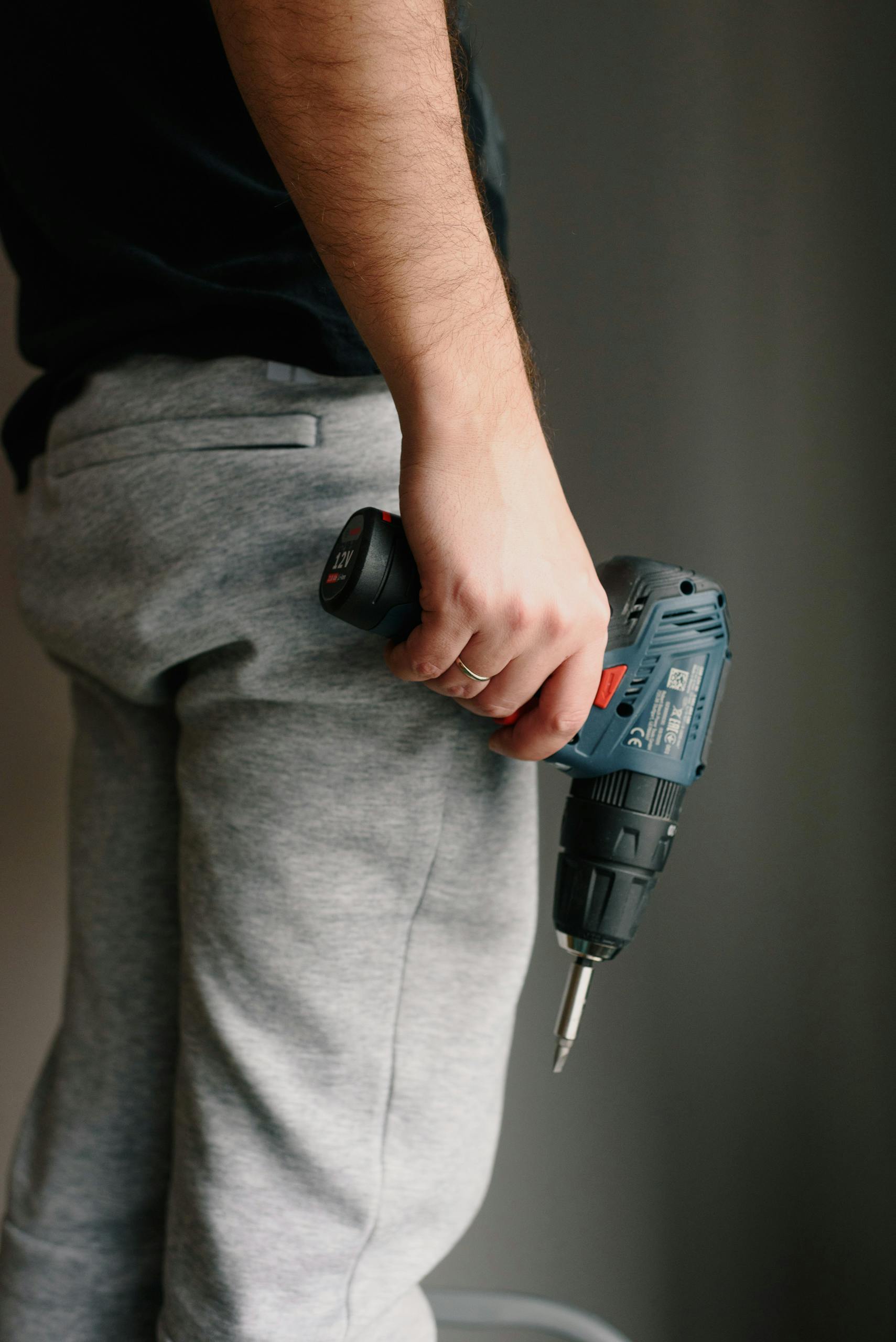 A man holds a cordless drill, ready for installing a ring alarm, against a neutral indoor background.